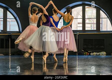 Four young female ballet dancers dressed in colorful tutus rehearse for a performance in a rehearsal hall Stock Photo