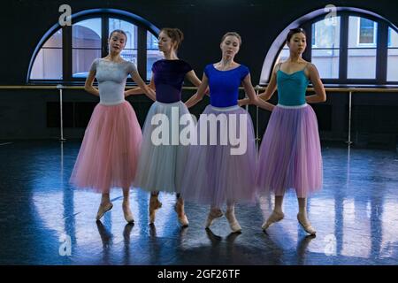 Four young female ballet dancers dressed in colorful tutus rehearse for a performance in a rehearsal hall Stock Photo