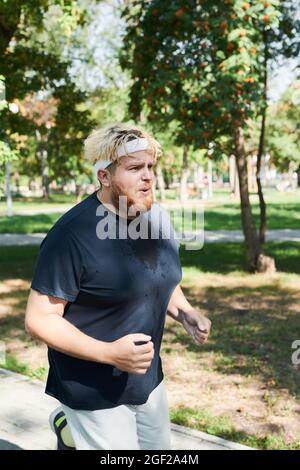 Young overweight man running outdoors in the park during his sport training Stock Photo