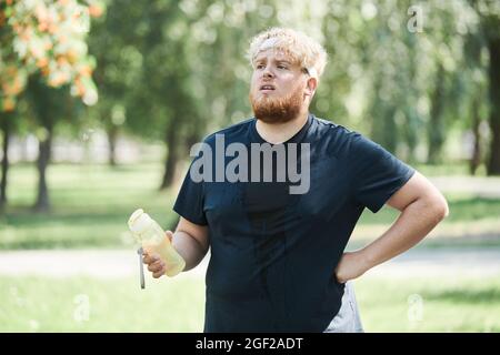 Overweight young man tired after sports training he drinking water while standing outdoors Stock Photo