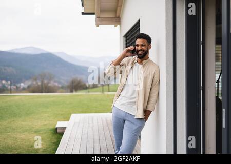 Young man student with smartphone outdoors on patio at home, making a phone call. Stock Photo