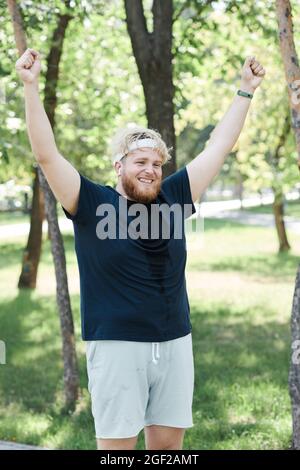 Overweight young man raising his arms and smiling he finishing his training and reaching a good results Stock Photo