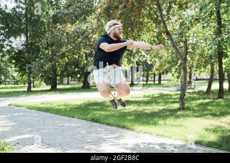 Overweight young man jumping during his sports training in the park in sunny day Stock Photo