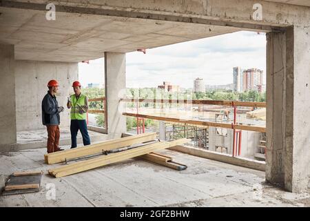 Wide angle view at two construction workers wearing hardhats while standing at construction site, copy space Stock Photo