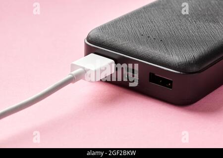 USB connector is connected to Power bank on a pink background. Charging gadgets. Close-up, selective focus Stock Photo