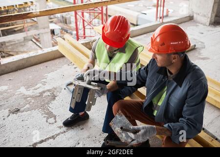 High angle view at two construction workers wearing hardhats while examining metal parts at construction site Stock Photo