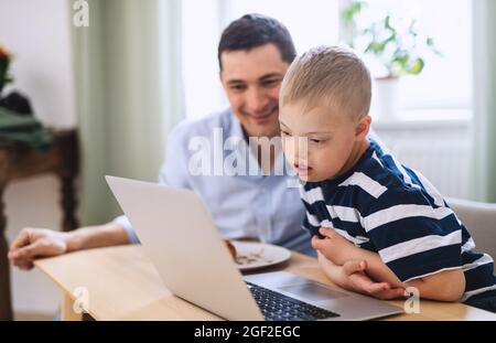 Father with happy down syndrome son indoors at home, using laptop. Stock Photo