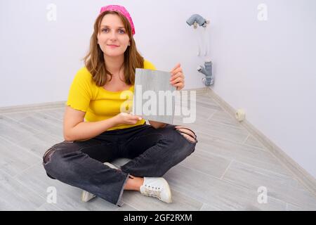 Woman installs floor tiles at home, DIY repair herself Stock Photo