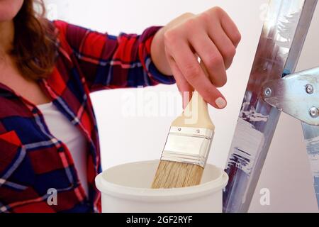 Woman hand, brush and can of white paint on stepladder Stock Photo