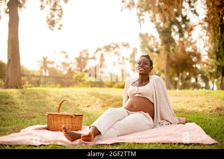 Delighted pregnant black woman relaxing in park
