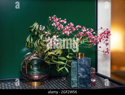 Dried flowers branch putted into elegant glass vase with decorative elements on the metal shelf in room. Modern design elements Stock Photo