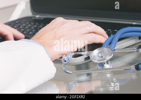 Close up of doctor's hands typing on a laptop with stethoscope in the foreground Stock Photo