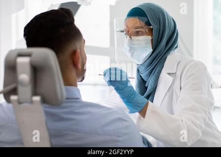 Islamic Dentist Lady In Medical Mask Checking Male Patient's Teeth In Clinic Stock Photo