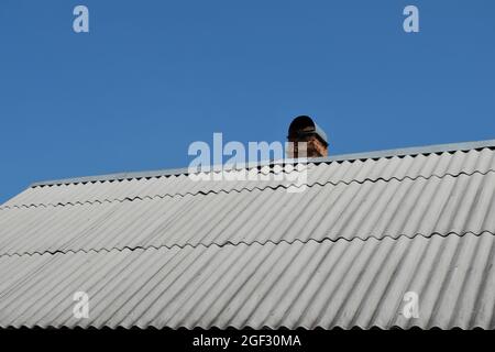 A brick chimney for stove heating on the roof of a village house. Wood-burning heating of a country house. Selective focus. Stock Photo