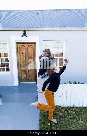 Brother and sister outside their home, boy dancing barefoot on grass. Stock Photo