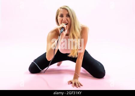 Beautiful young woman with microphone singing on pink background  Stock Photo