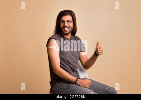 Cheerful indian guy showing thumb up, got vaccinated against COVID-19 Stock Photo