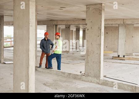 Full length portrait of two workers discussing engineering at costruction site, copy space Stock Photo