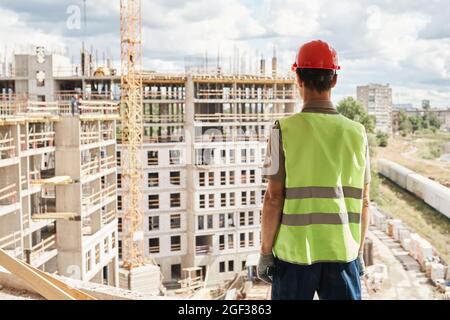 Back view at construction worker wearing hardhat while standing at high rise building, copy space Stock Photo