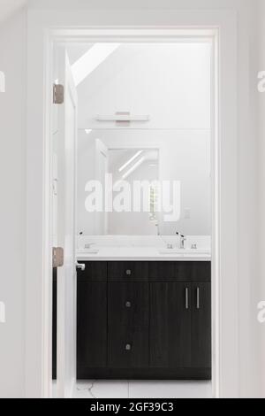 Looking towards a bathroom through the door way with a dark wood vanity cabinet, white granite countertop, and light above the mirror. Stock Photo