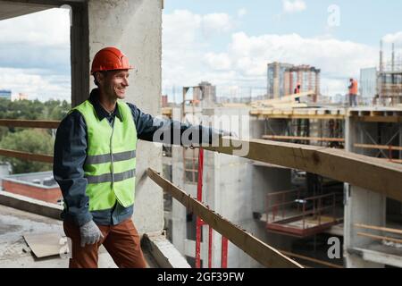 Waist up portrait of young man working at construction site and looking at cityskape, copy space Stock Photo