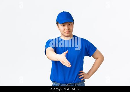 Friendly cheerful asian courier in blue uniform smiling confident, extend hand for handshake, greeting customer, making deal. Delivery man saying Stock Photo