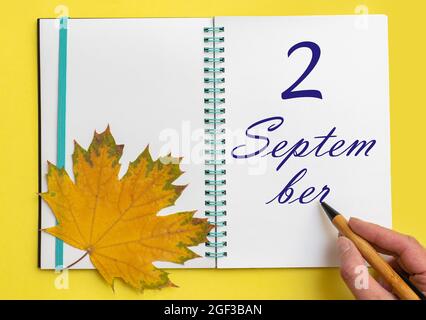 2nd day of september. Hand writing the date 2 september in an open notebook with a beautiful natural maple leaf on a yellow background. Autumn month, Stock Photo