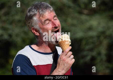 Middle aged British grey haired man in his fifties eating an ice cream cone Stock Photo