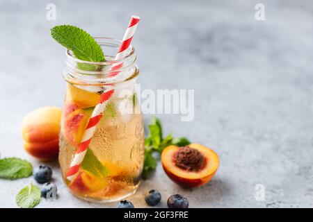 Cold peach blueberry ice tea in jar with drinking straw. Copy space. Refreshing summer lemonade Stock Photo