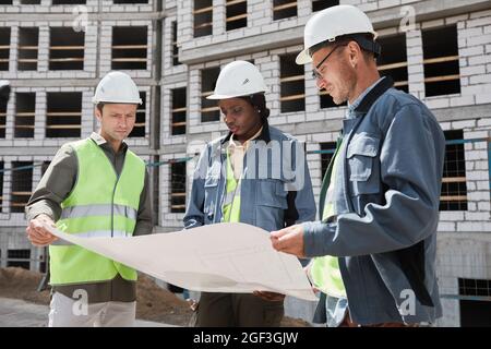 Waist up shot of diverse group of engineers discussing floor plans at construction site Stock Photo