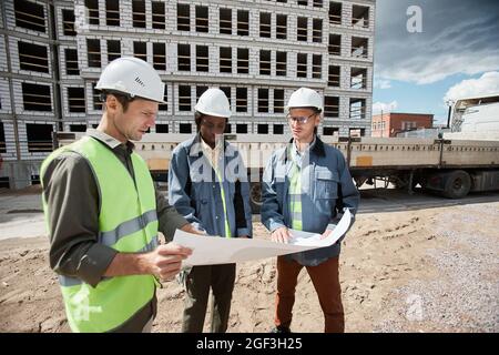 Diverse group of engineers discussing floor plans at construction site, copy space Stock Photo