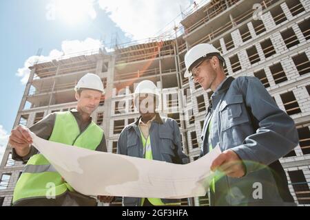 Low angle view at diverse group of engineers discussing floor plans at construction site Stock Photo