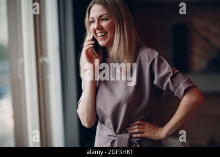 Business woman young adult coach standing at office window and speaking on mobile phone Stock Photo