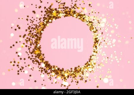 Round frame made of gold colored stars confetti on a pink pastel background. Stock Photo