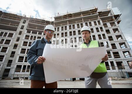 Low angle portrait of two engineers discussing floor plans at construction site, copy space Stock Photo
