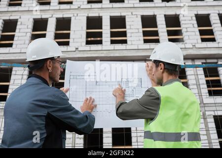 Back view portrait of two engineers discussing floor plans at construction site Stock Photo