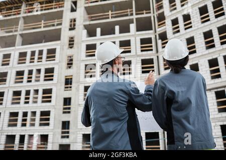Back view portrait of two engineers discussing floor plans at construction site, copy space Stock Photo