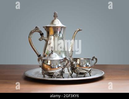 Ornate 4-piece tea set on table. Silver or silver plated tea pot, sugar bowl and cream or milk jug. Ornamental silverware to serve hot tea or coffee. Stock Photo