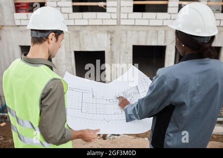 Back view portrait of two workers discussing floor plans at construction site, copy space Stock Photo