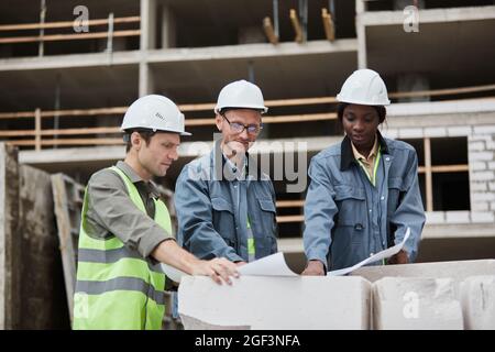 Waist up portrait of workers discussing floor plans at construction site, copy space Stock Photo