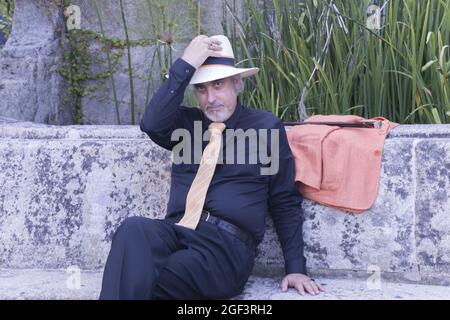 Handsome gray-haired male model sitting on a stone bench Stock Photo