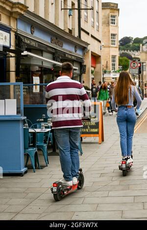 Bath, England - August 2021: Two people riding through a pedestrianised area on an e-scooter in the city centre Stock Photo