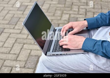 Laptop computer and man hands while working remotely on the computer outdoors.  Freelance programmer works remotely outdoors. Computer for learning Stock Photo