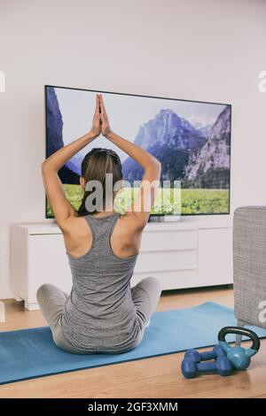 Yoga at home fitness class streaming on TV app online woman training in living room on exercise mat meditating alone - workout lifestyle Stock Photo
