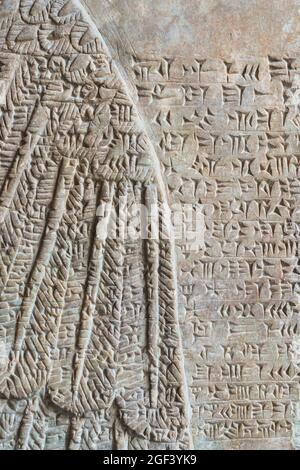 ancient Assyrian cuneiform carved on stone wall over sphinx wing relief Stock Photo
