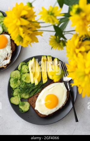 Delicious breakfast with avocado, fresh cucumbers and microgreens of peas with dill, fried eggs on black grain toast Stock Photo