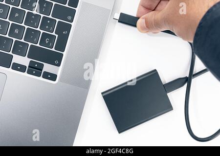 Hand connecting a External hard disk to a modern laptop computer. Top view Stock Photo