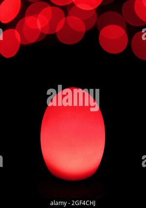 Shining Scarlet Red Egg Shaped Table Lamp with Bokeh Light on Dark Background Stock Photo