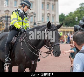 London, UK. 23 August 2021. Crowds outside Buckingham Palace to watch Changing the Guard after the longest pause since WW2 due to the Coronavirus restrictions in March 2020. Number 3 Company from 1st Battalion Coldstream Guards undertake this first full ceremonial duty. Visitors pat a Metropolitan mounted police horse during a lull in the ceremony. Credit: Malcolm Park/Alamy Stock Photo