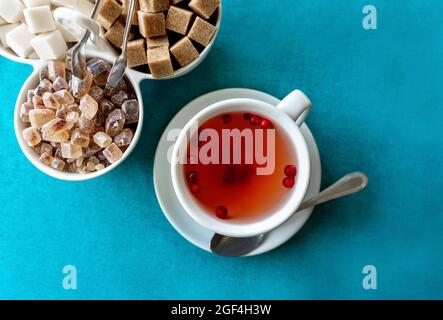 Red herbal tea with cranberries in ceramic white cup with white and cane sugar on blue tablecloth. Food background with copy space. Flat lay style. Food and drink concept. Stock Photo